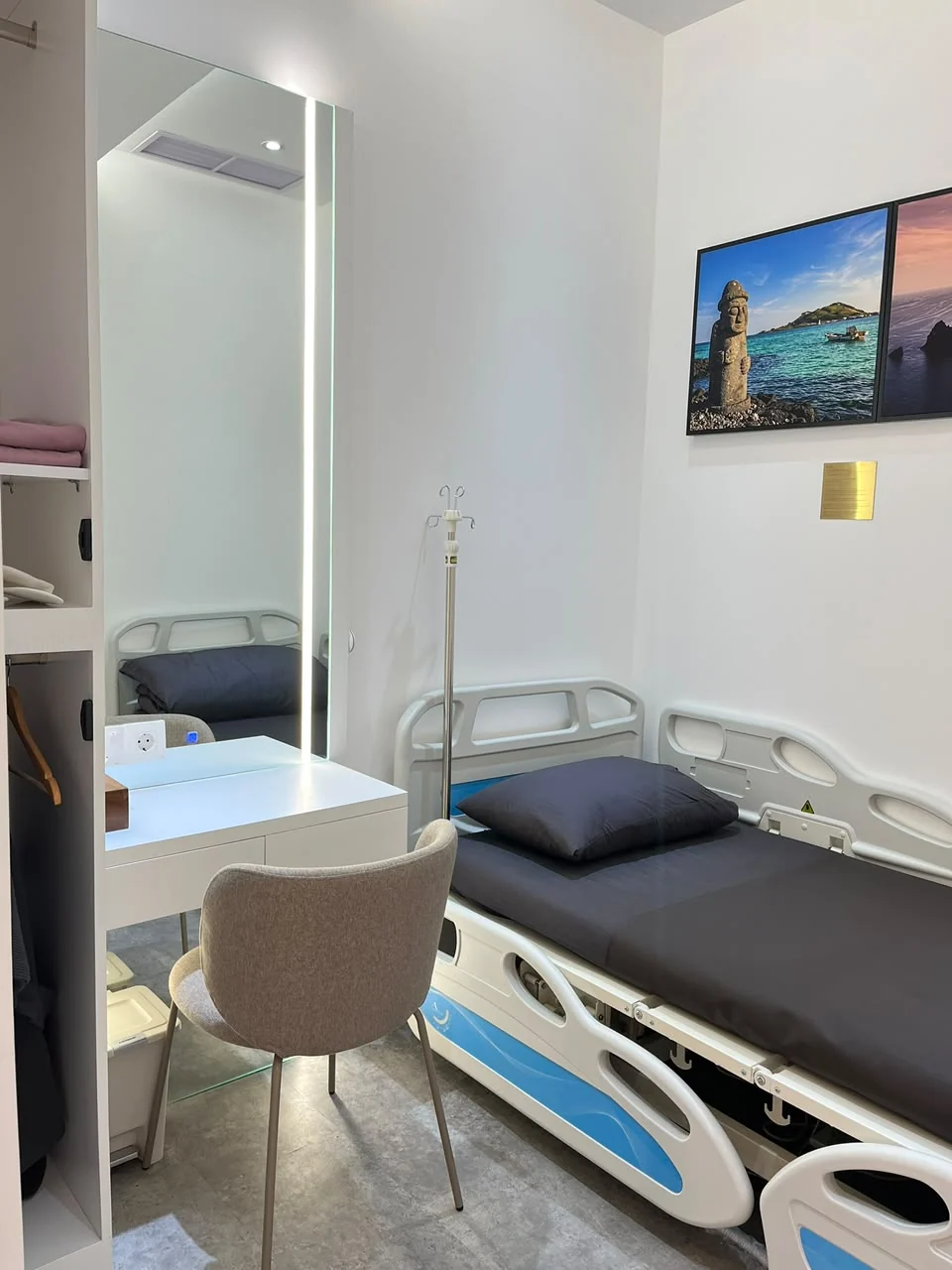 Sudut ruang VIP Hestia Women Clinic dengan tempat tidur medis, vanity custom, cermin full-height dengan pencahayaan vertikal, kursi, dan artwork dinding.